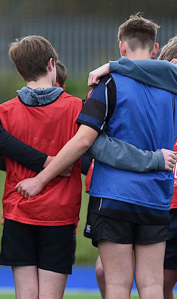 Shop Gifts for Kids Now young Rugby players with arms around each other in a huddle, listing intently to their coach