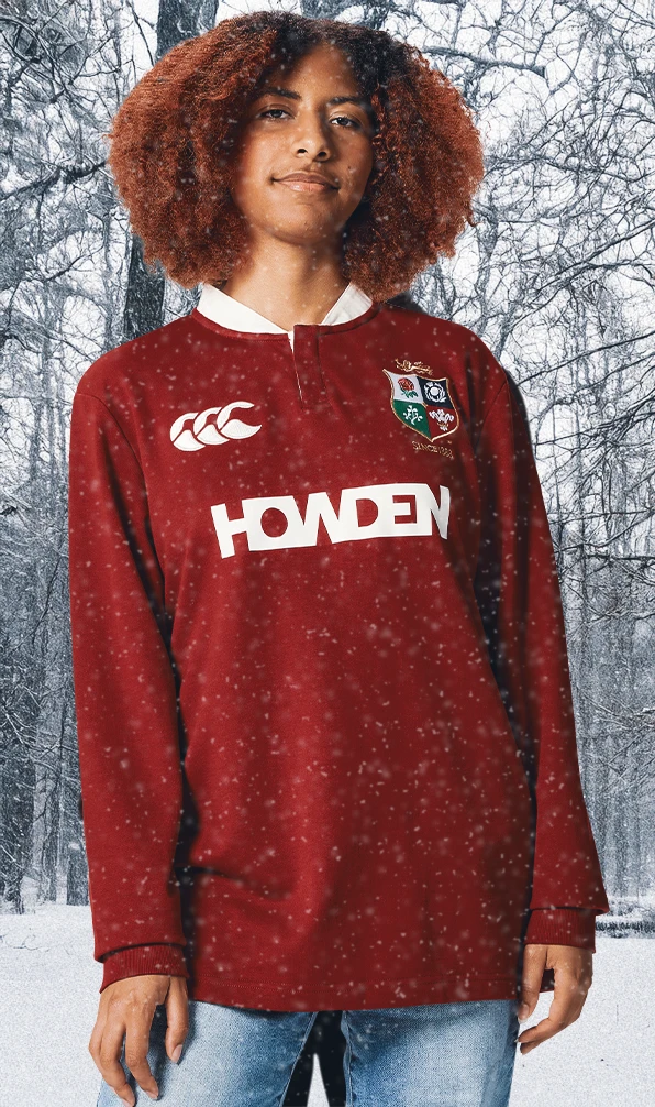 A womens stats looking into the camera, wearing a British & Irish Lions rugby jersey. She stands in front of a snowy woodland scene while snow gently falls