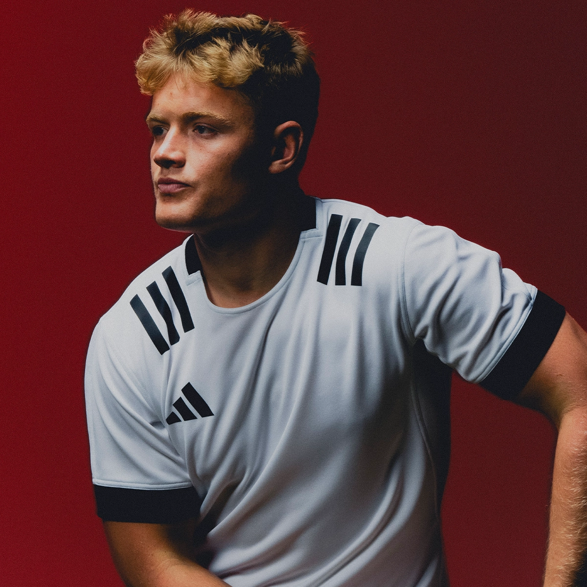 A rugby player is posing in a white Adidas rugby shirt.
