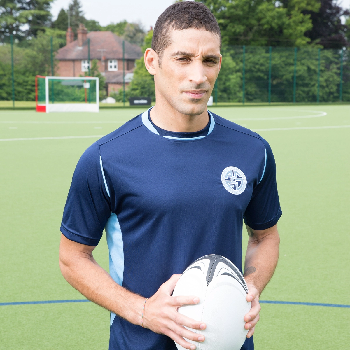 A rugby player holds the ball while posing in his club training wear