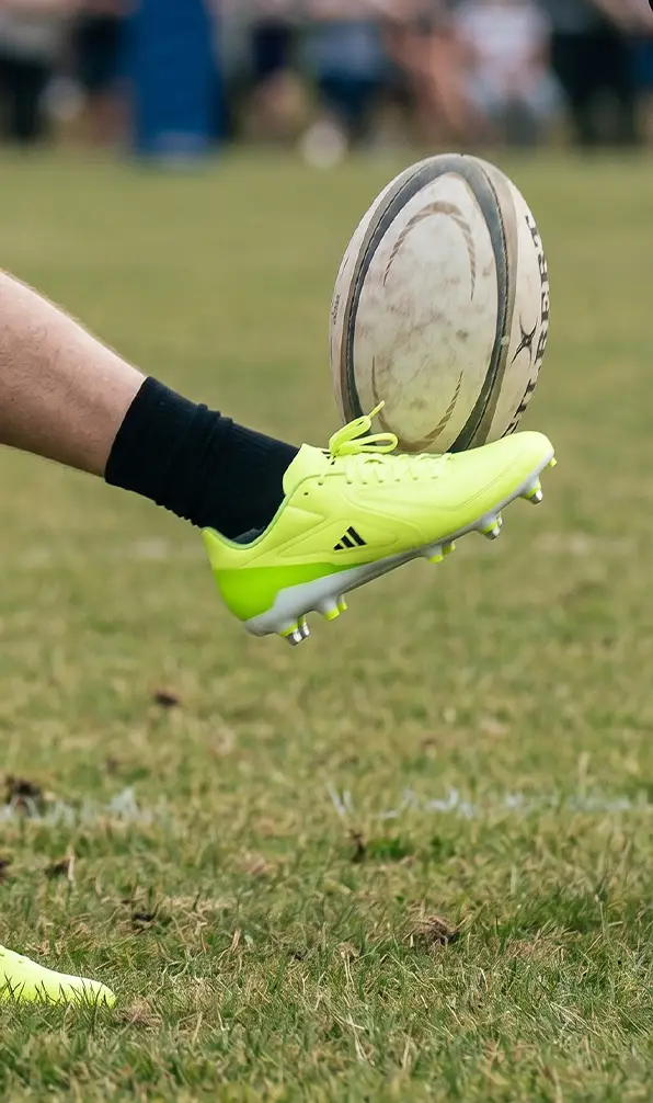 A back is in the motion of kicking a ball in his pair of Adidas rugby boots.