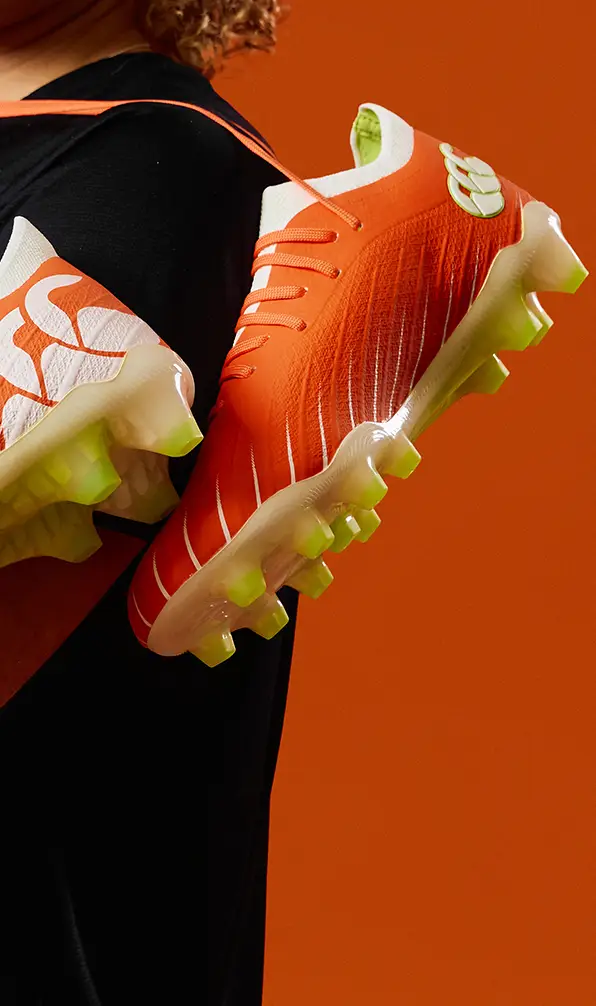 A close up image of a pair of orange Canterbury rugby boots over someone's shoulder