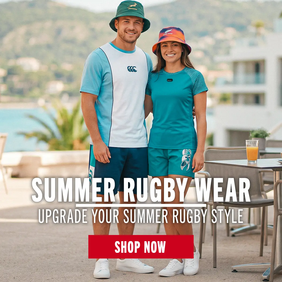 A young man and woman stand side by side wearing summer rugby styled clothing. They have their arms round one-another and are standing in a very sunny mediterranean spot.