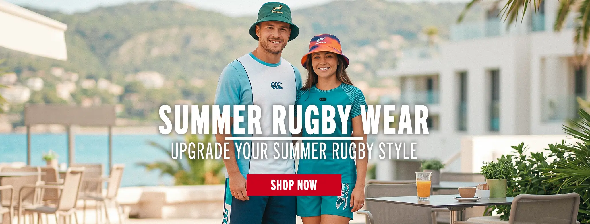 A young man and woman stand side by side wearing summer rugby styled clothing. They have their arms round one-another and are standing in a very sunny mediterranean spot.