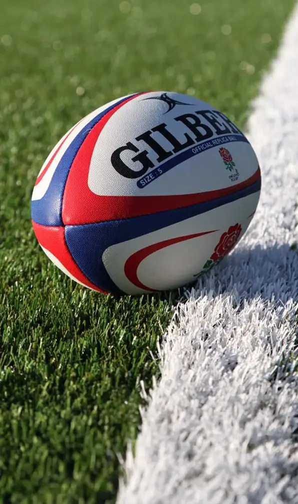 An England rugby ball is sitting on the side of a rugby pitch.