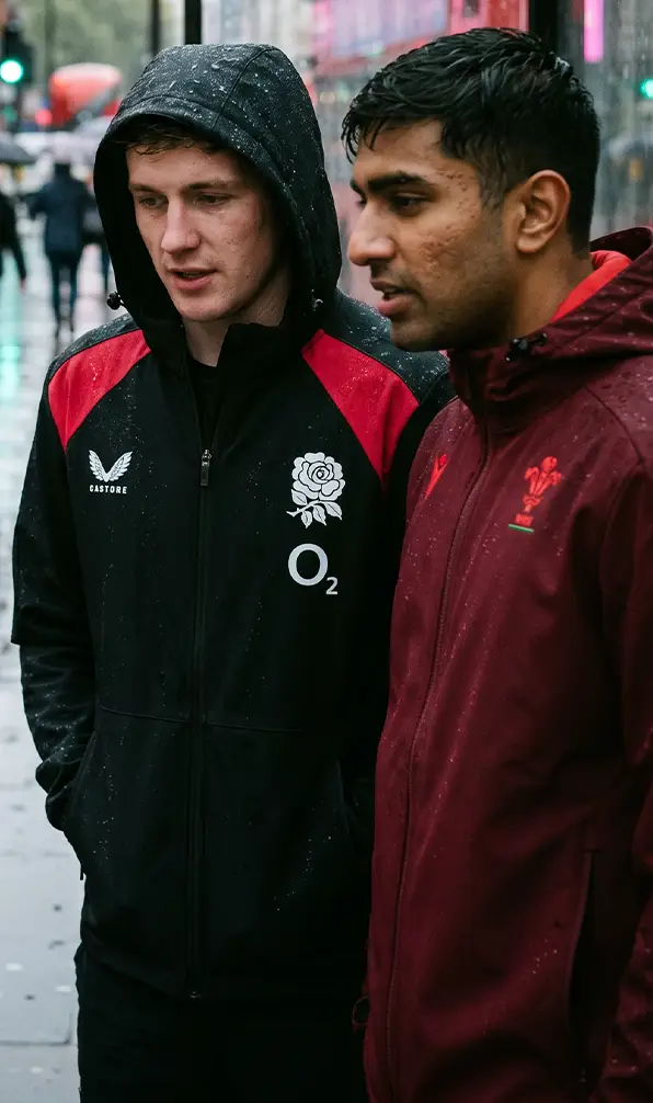 Two guys are standing under a bus stop wearing England and Wales jackets.