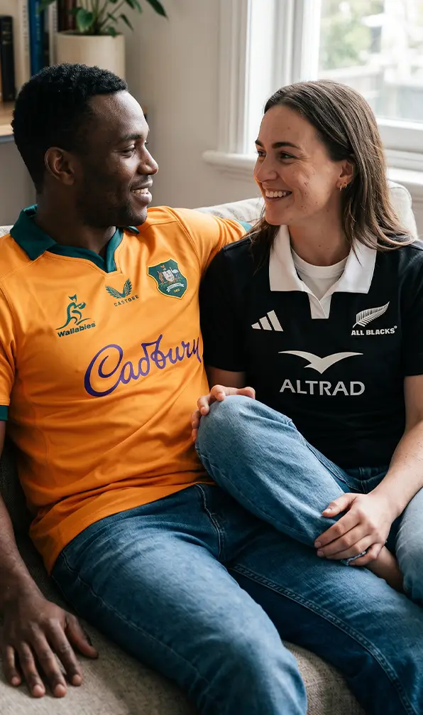 A man and a women sitting on a sofa wearing the Australia and All Blacks rugby shirts.