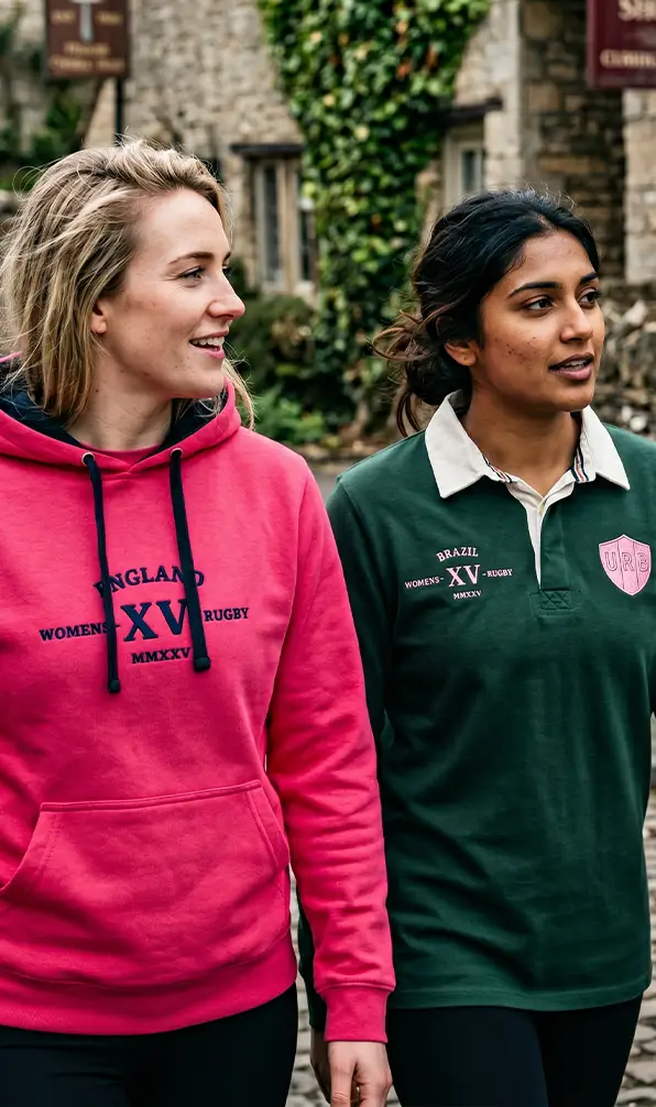 Two women are walking through a village in a classic Womens Rugby World Cup hoodie and a Brazil Classic rugby shirt.