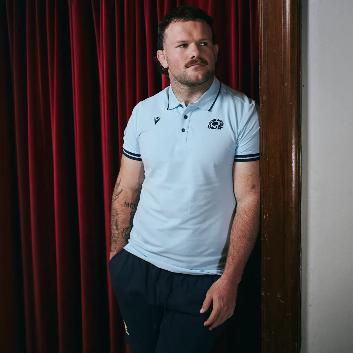 Scotland Travel Reveal Ewan Ashman stands wearing the new Scotland travel polo.