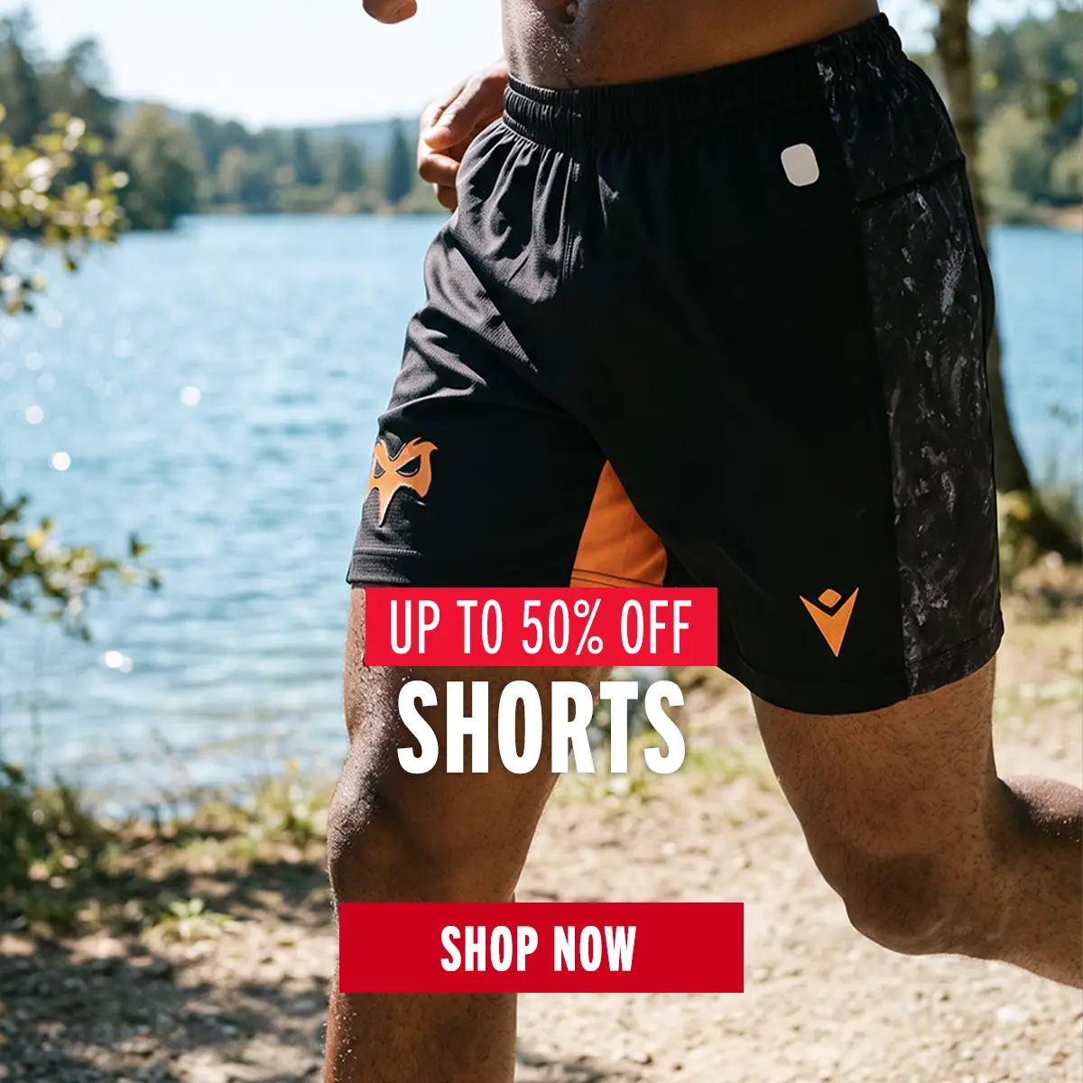 A man is running by a lake in his Ospreys rugby shorts.