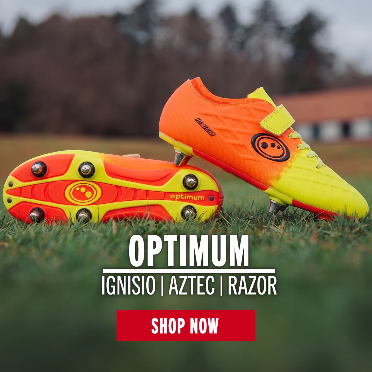 A pair of Optimum Ignisio rugby boots are placed one on tip of the other on a grass pitch.